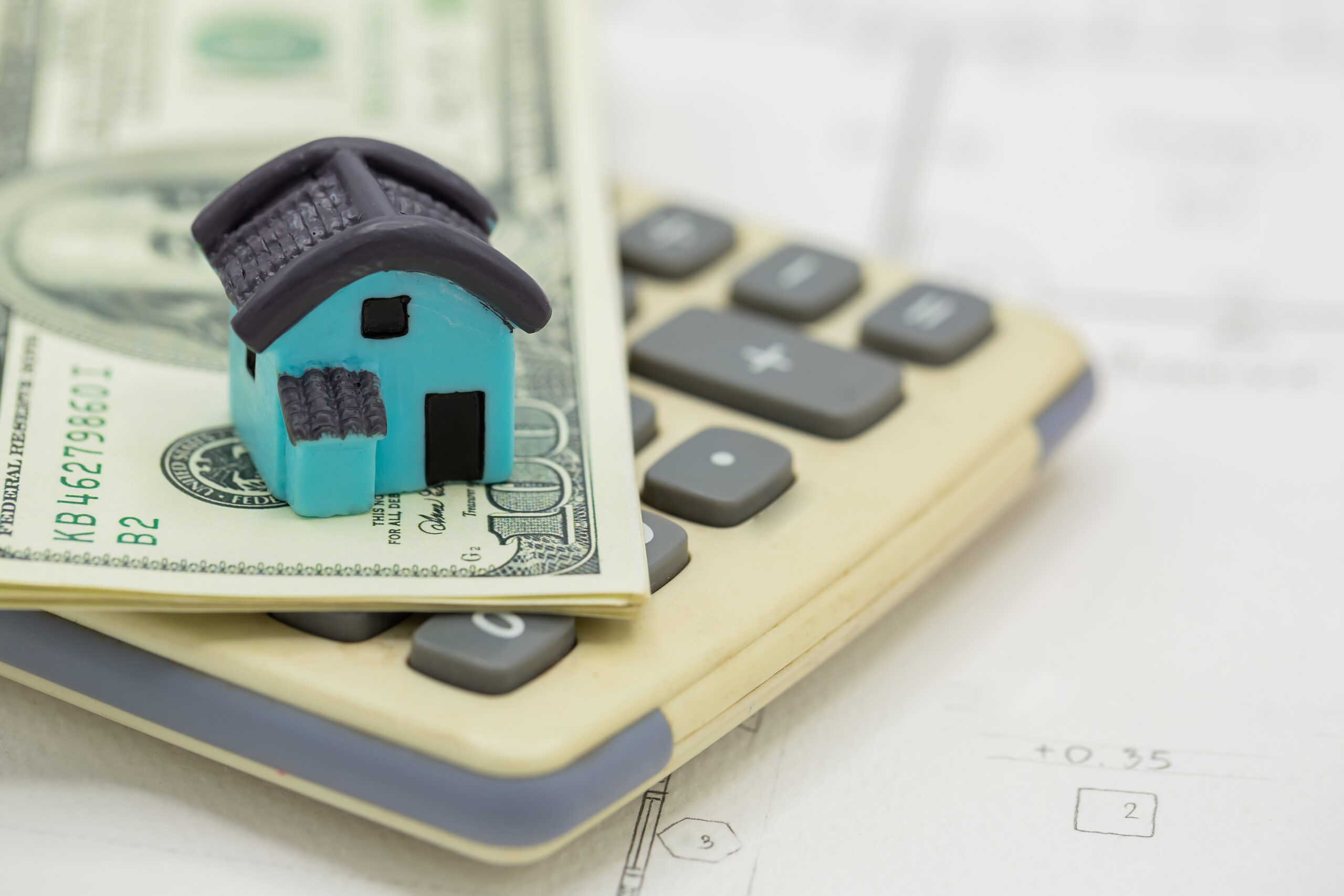 a sculpture of a small house on a calculator and a dollar bill